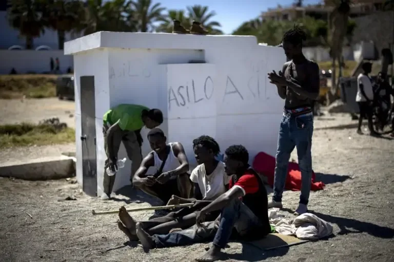 Several immigrants of sub-Saharan origin, on Trampolín beach, next to a graffiti asking for asylum.
